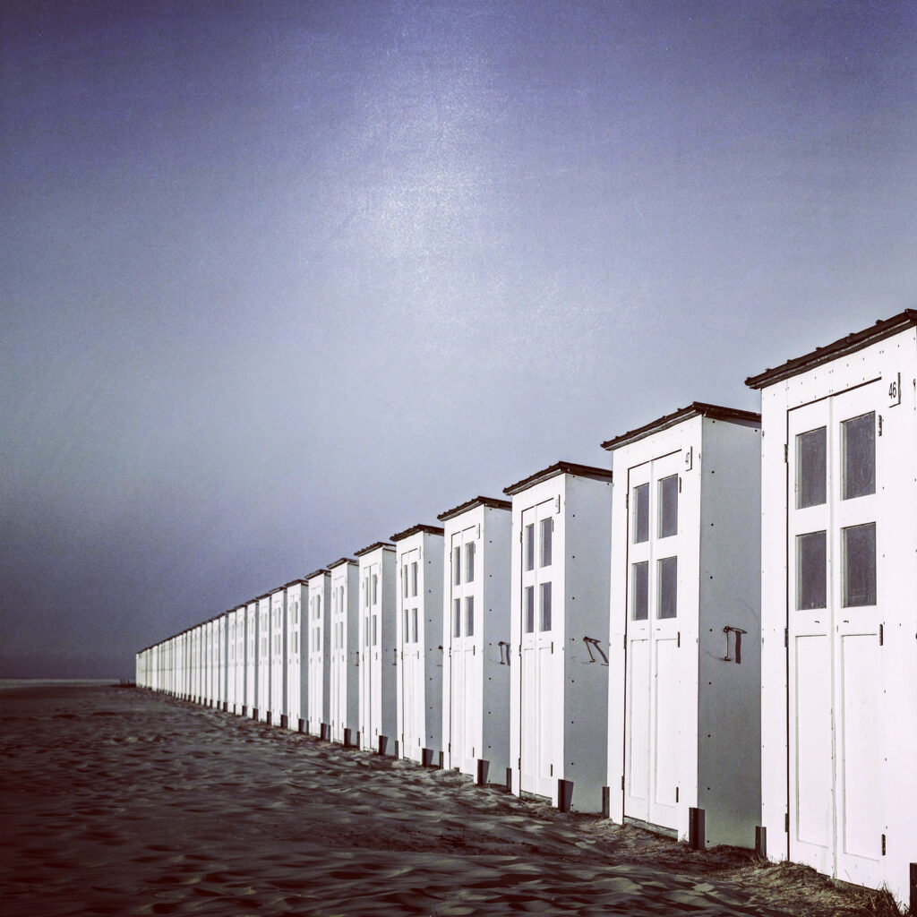 Een haast oneindige rij van witte strandhuisjes waarvan de vierkante raampjes uit lijken te kijken op oneindigheid